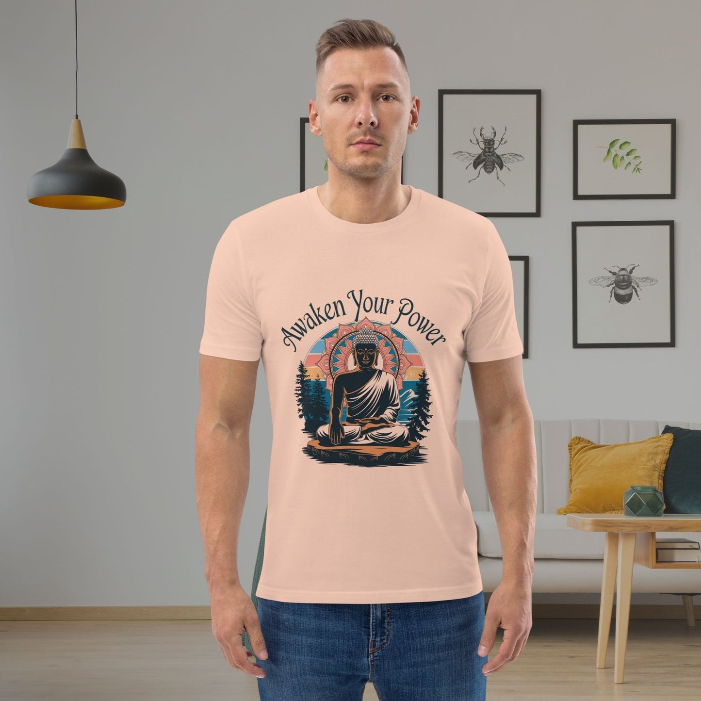 Man wearing a peach t-shirt with a Buddha graphic and 'Awaken Your Power' text in a room with framed pictures on the wall.