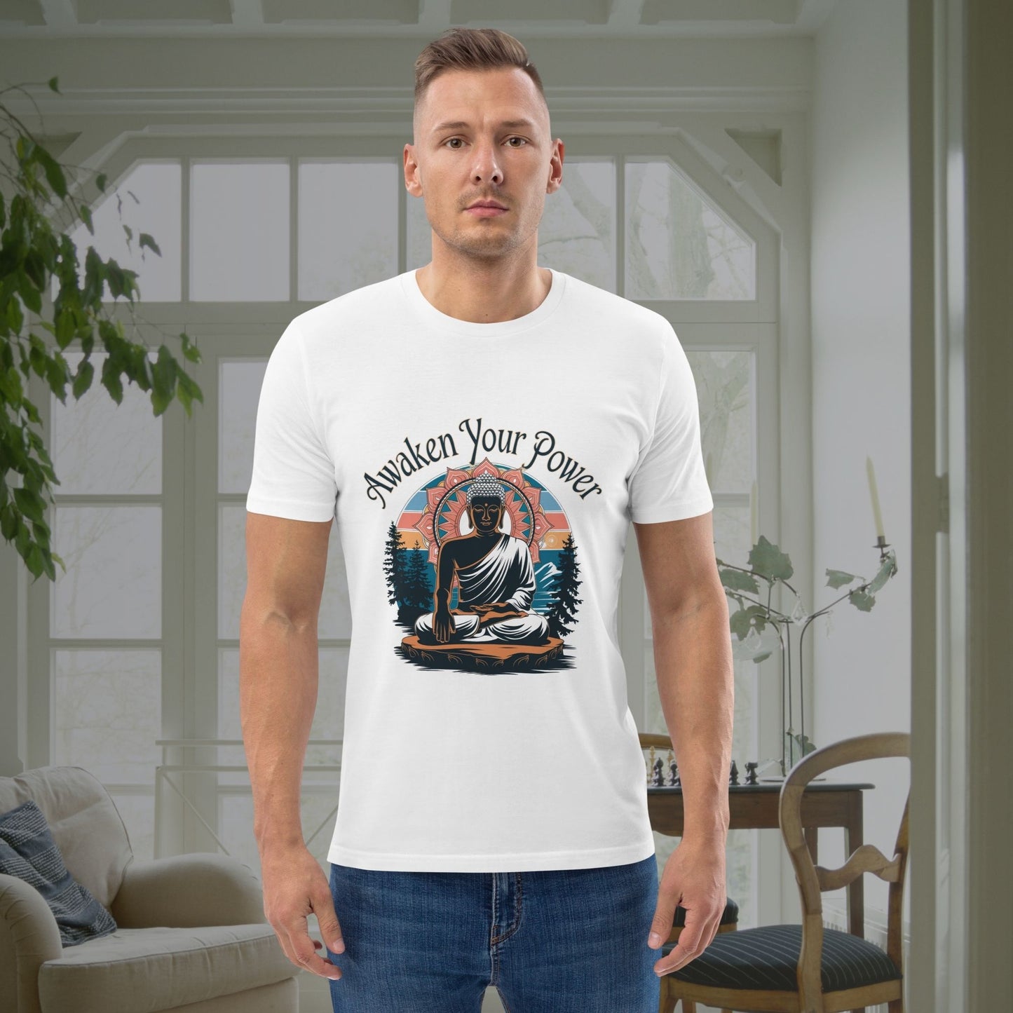 Man in a white graphic shirt with a peaceful, enlightened figure and landscape design, standing indoors