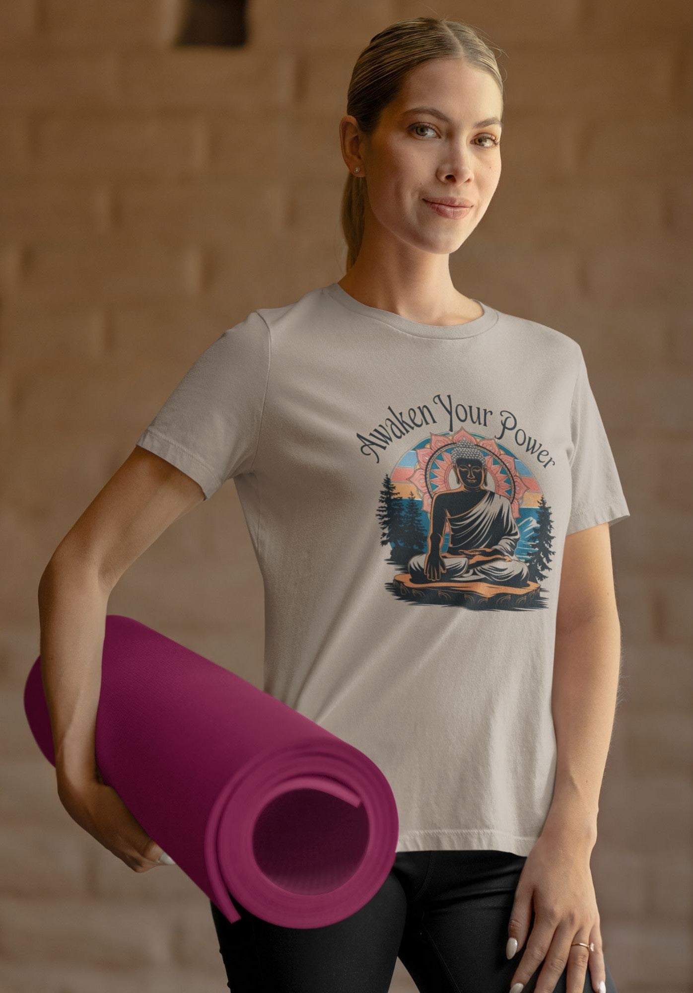 A woman wearing a mindful meditation t-shirt, featuring a Buddha graphic and "Awaken Your Power" text, holds a rolled-up magenta yoga mat, embodying a serene and active lifestyle.