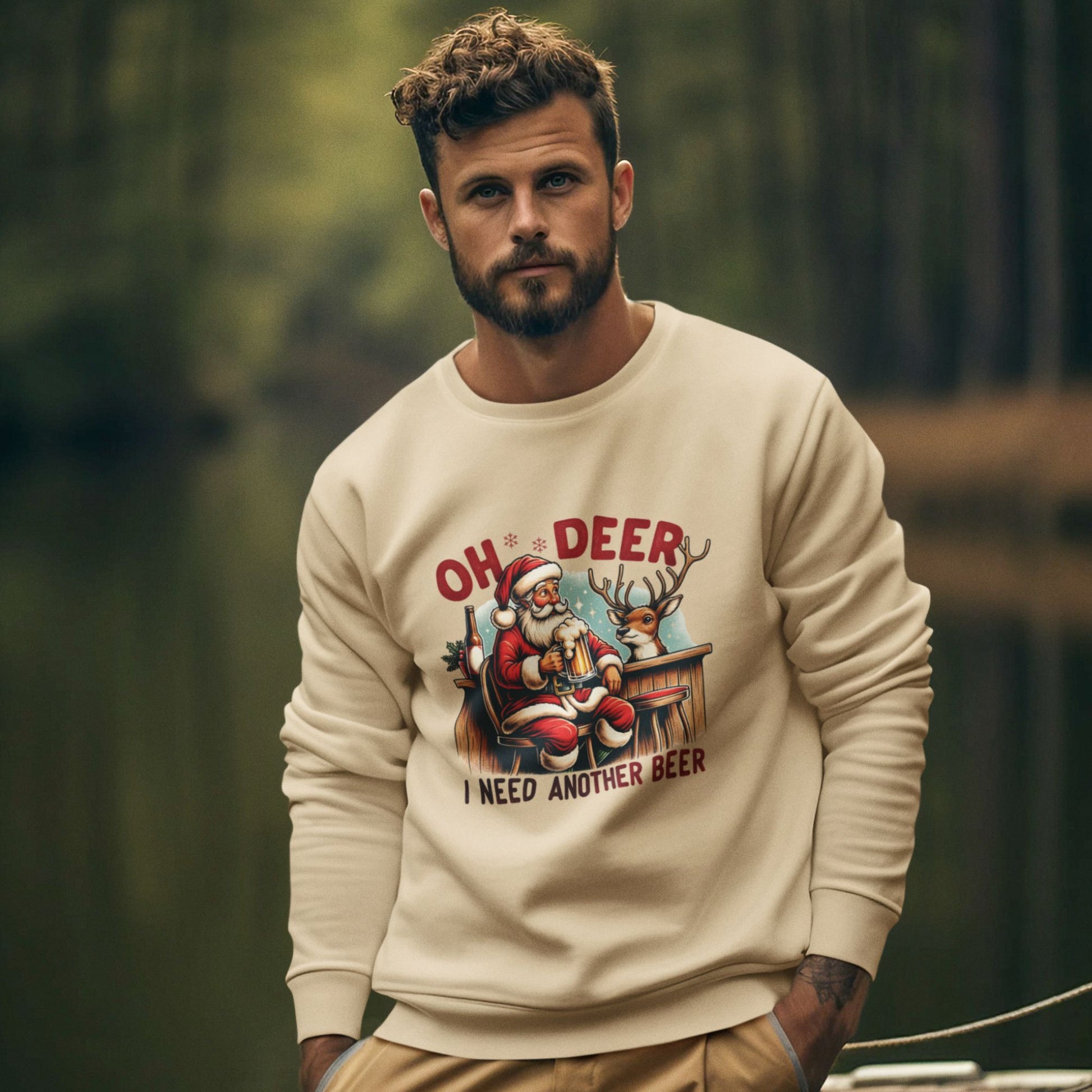 Bearded-man-wearing-a-cream-sweatshirt-with-a-Santa-and-reindeer-graphic-posing-in-a-serene-forest-setting-near-a-calm-lake