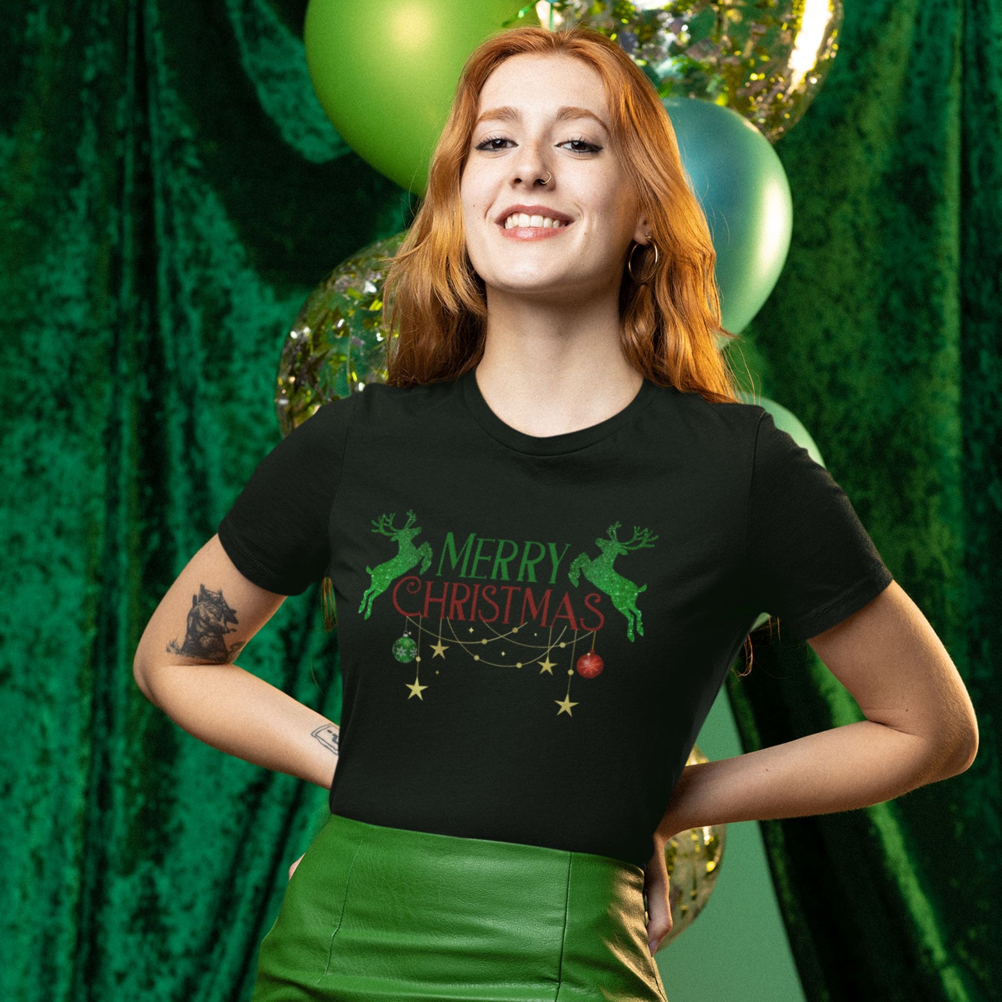 Charming-red-haired-woman-smiling-wearing-a-black-Christmas-themed-t-shirt-with-reindeer-graphics-posing-with-green-and-gold-balloons