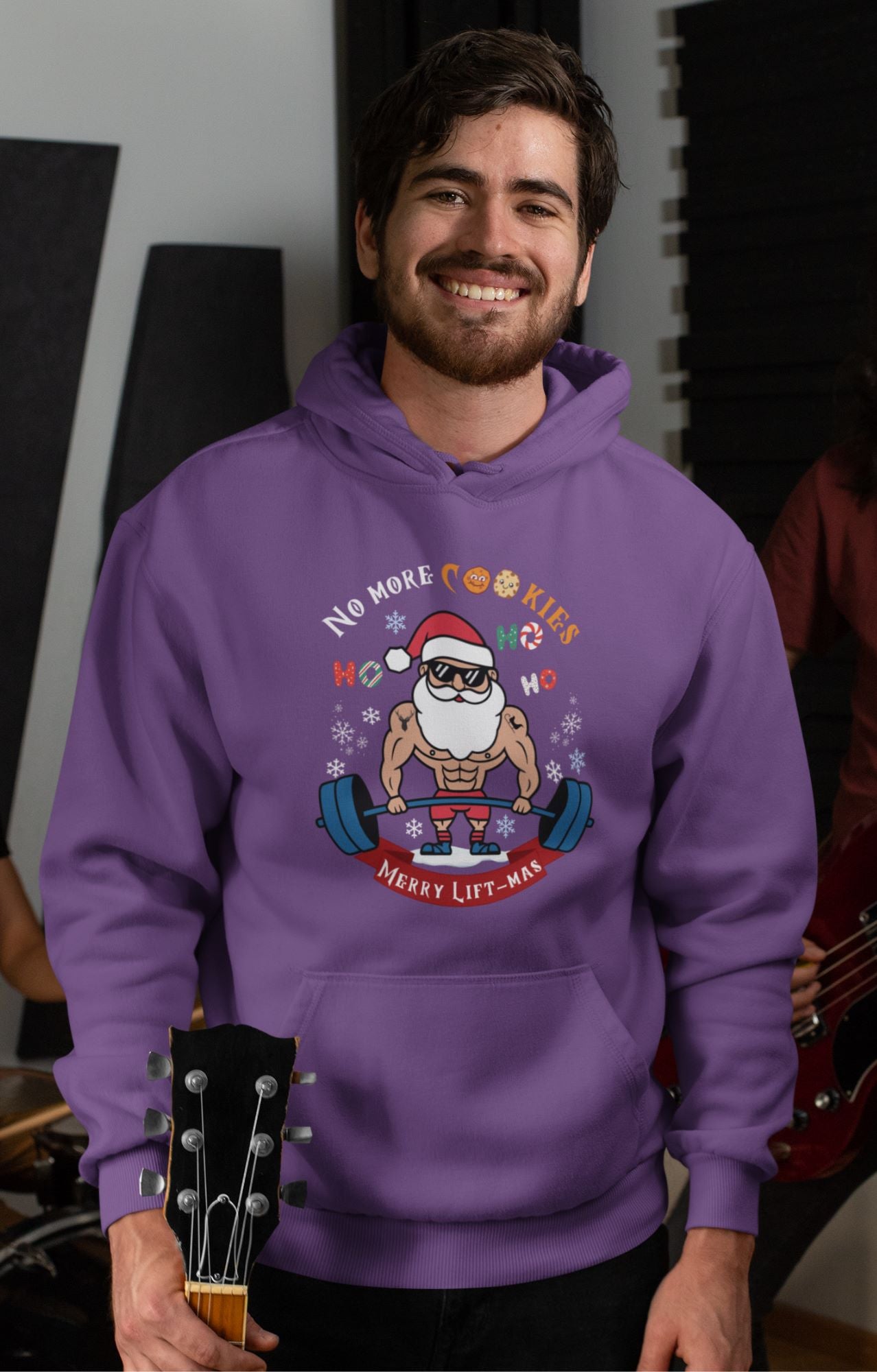 Guitarist-man-wearing-a-Christmas-themed-hoodie-featuring-a-weightlifting-Santa-design-with-snowflakes-and-holiday-decorations