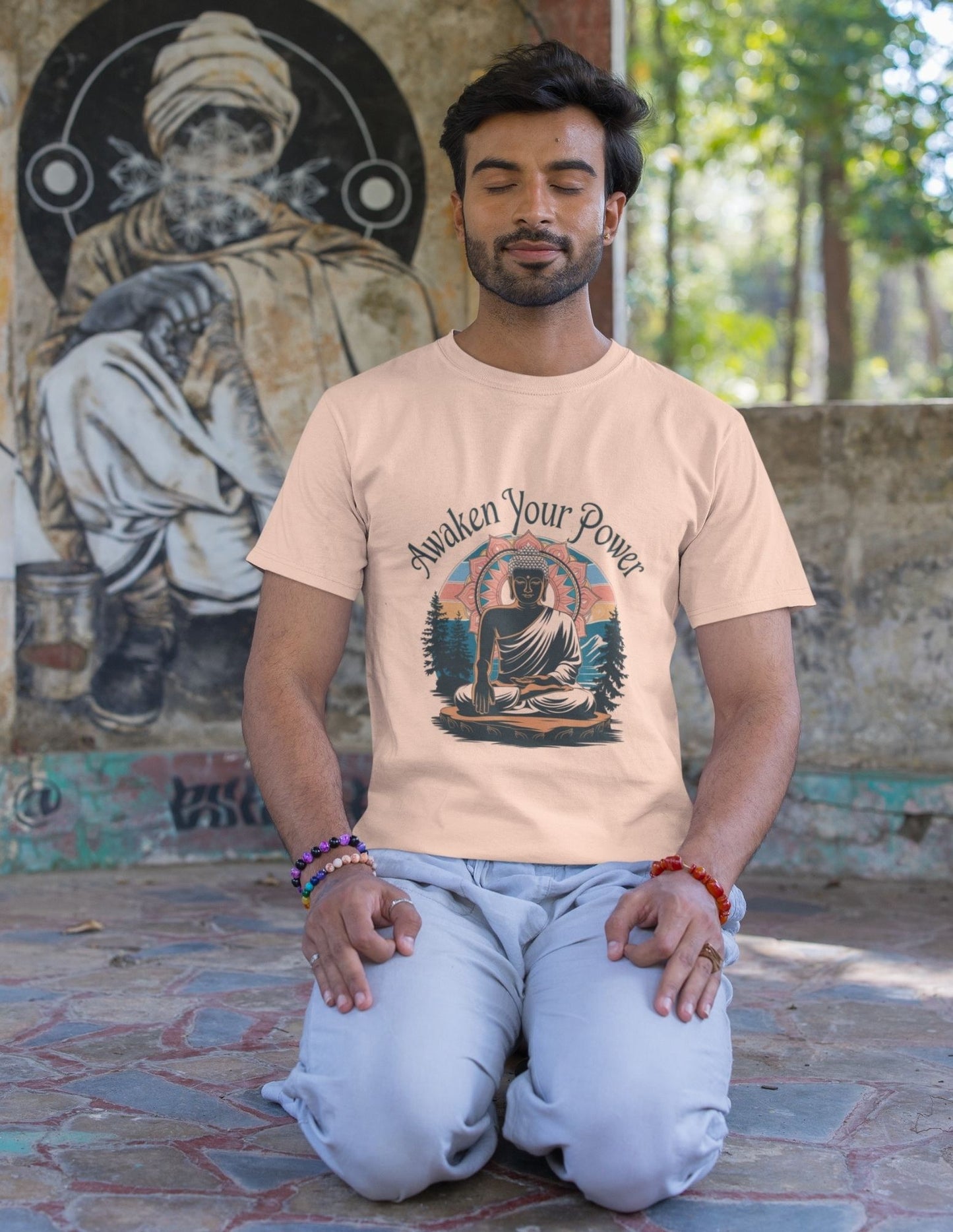 Man meditating in light orange graphic tee with a Buddha design, kneeling on patterned ground with mural behind