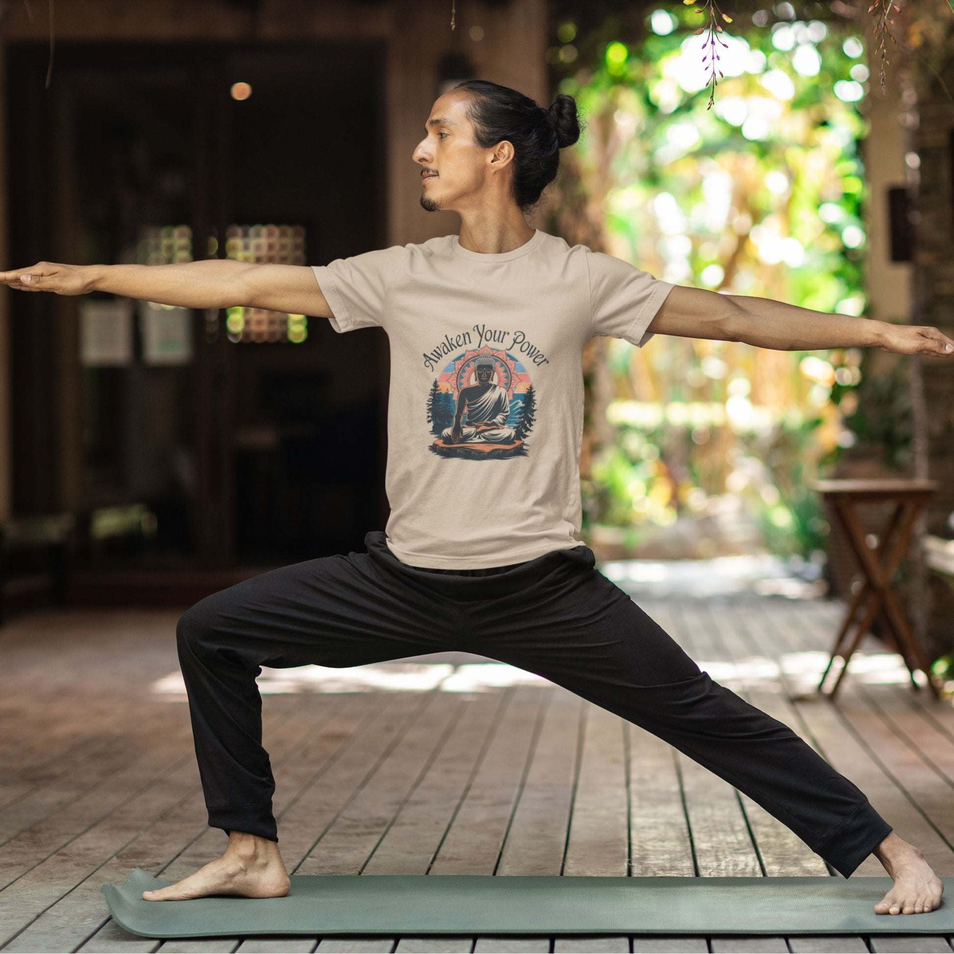 Man in tan 'Spiritual Awakening Tee' with Buddha design in warrior pose on a yoga mat, indoors with plants