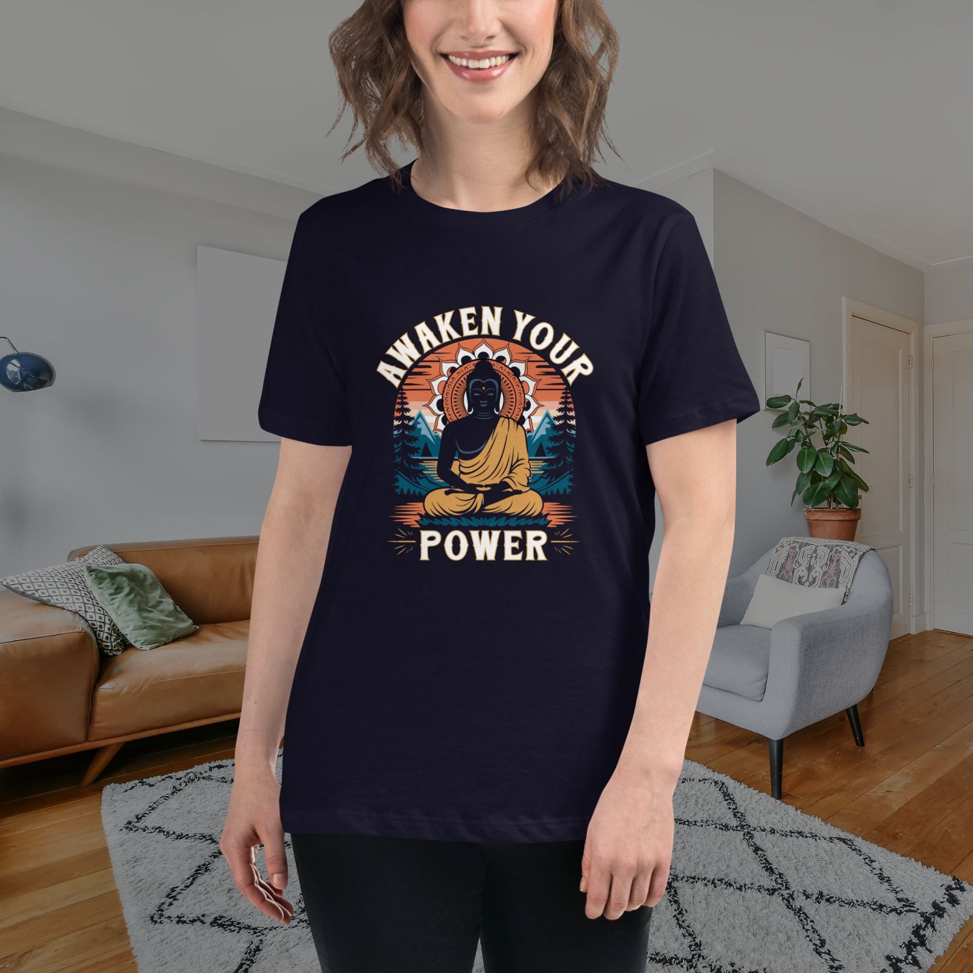 A smiling woman stands in a cozy living room, wearing a dark t-shirt featuring a stylized meditating figure and motivational text.