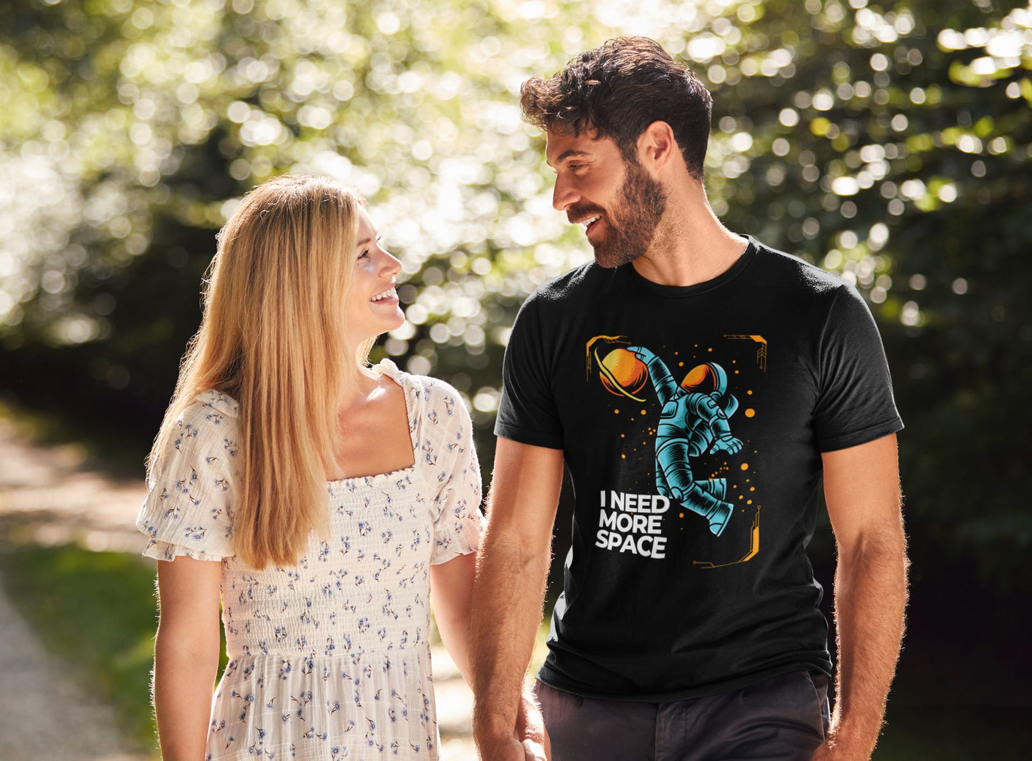 a-happy-man-and-his-girlfriend-surrounded-by-nature-the-man-wears-ablack-t-shirt-featuring-a-whimsical-blue-astronaut-floating-in-space