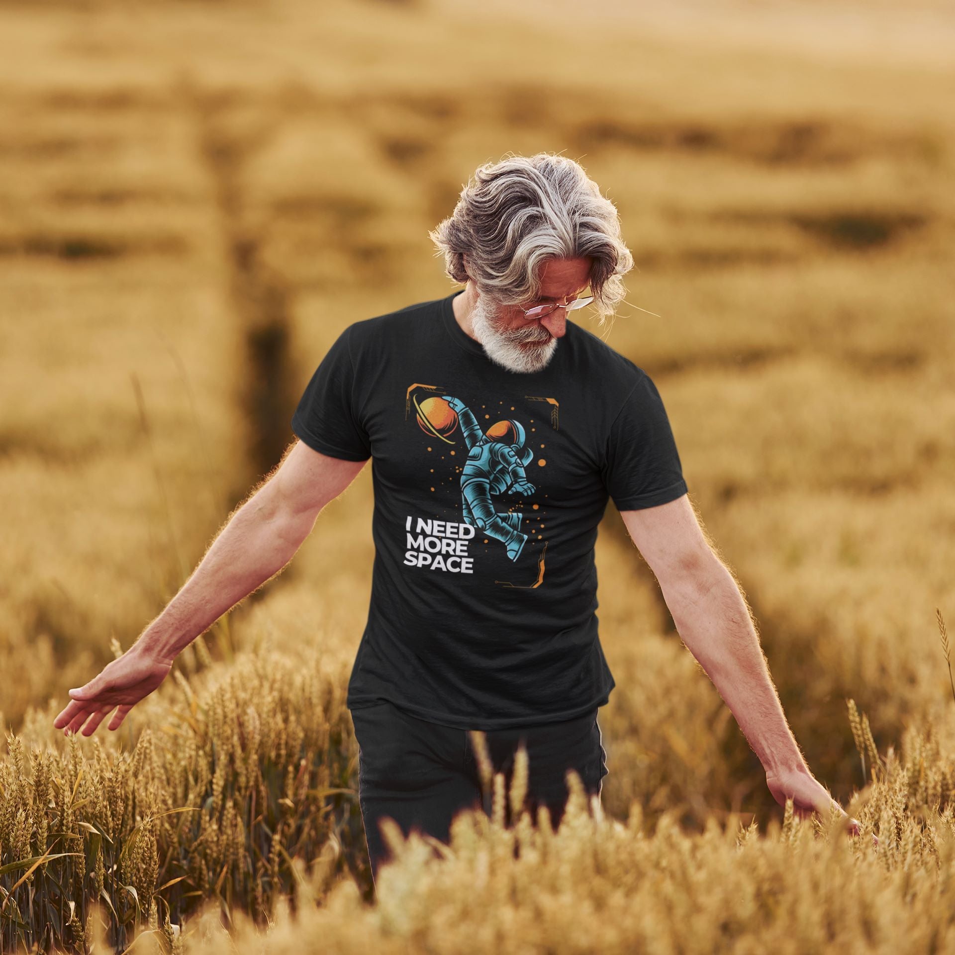 a-senior-man-walking-through-a-wheat-field-wearing-a-black-tee-with-a-cartoonish-blue-astronaut-design