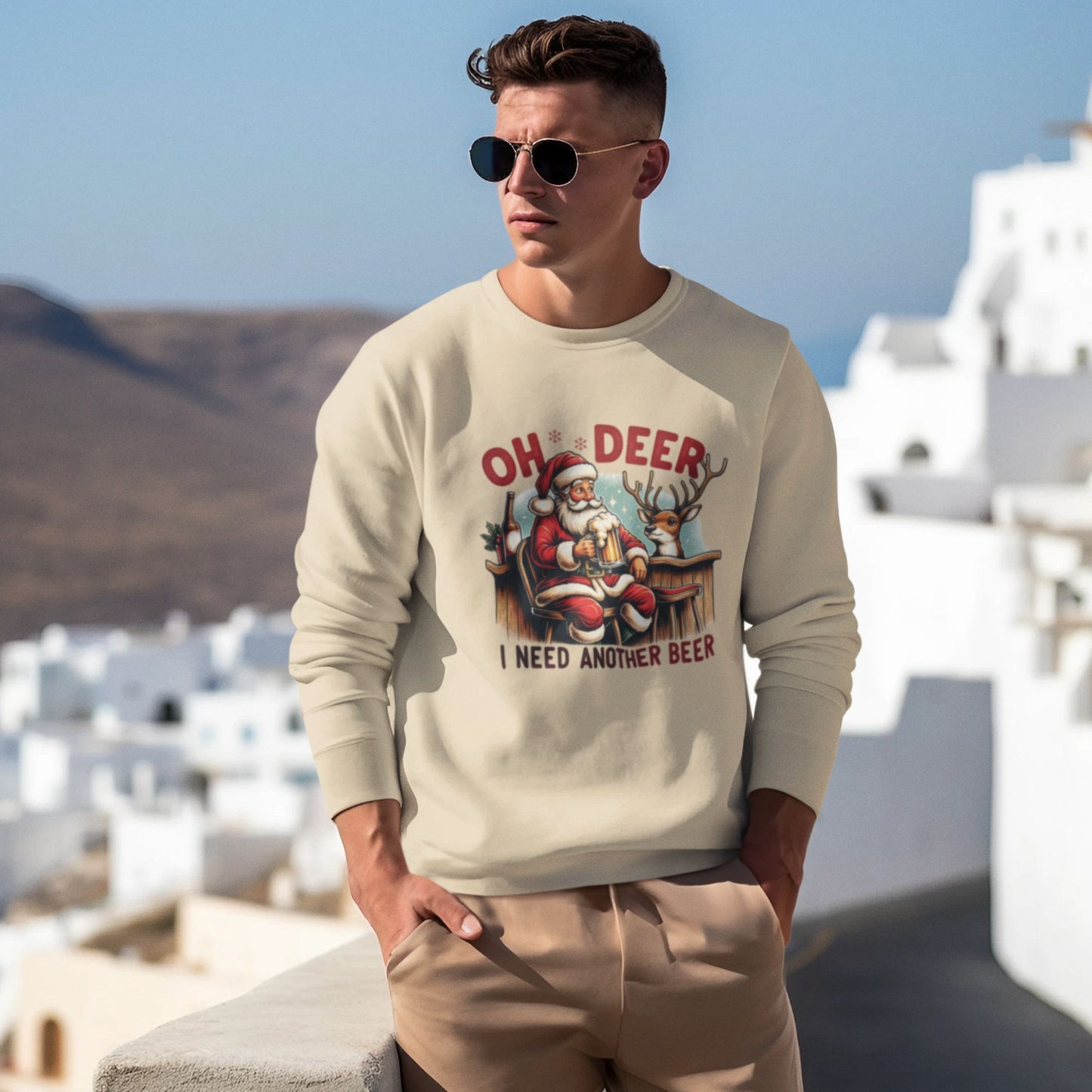 cream-sweatshirt-with-Santa-drinking-beer-and-reindeer-graphic-worn-by-a-man-standing-by-picturesque-Mediterranean-architecture