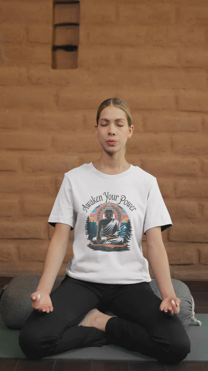 A woman meditates cross-legged on a mat, eyes closed and hands resting on her knees. She wears a white "Zen Power" t-shirt featuring an image of Buddha