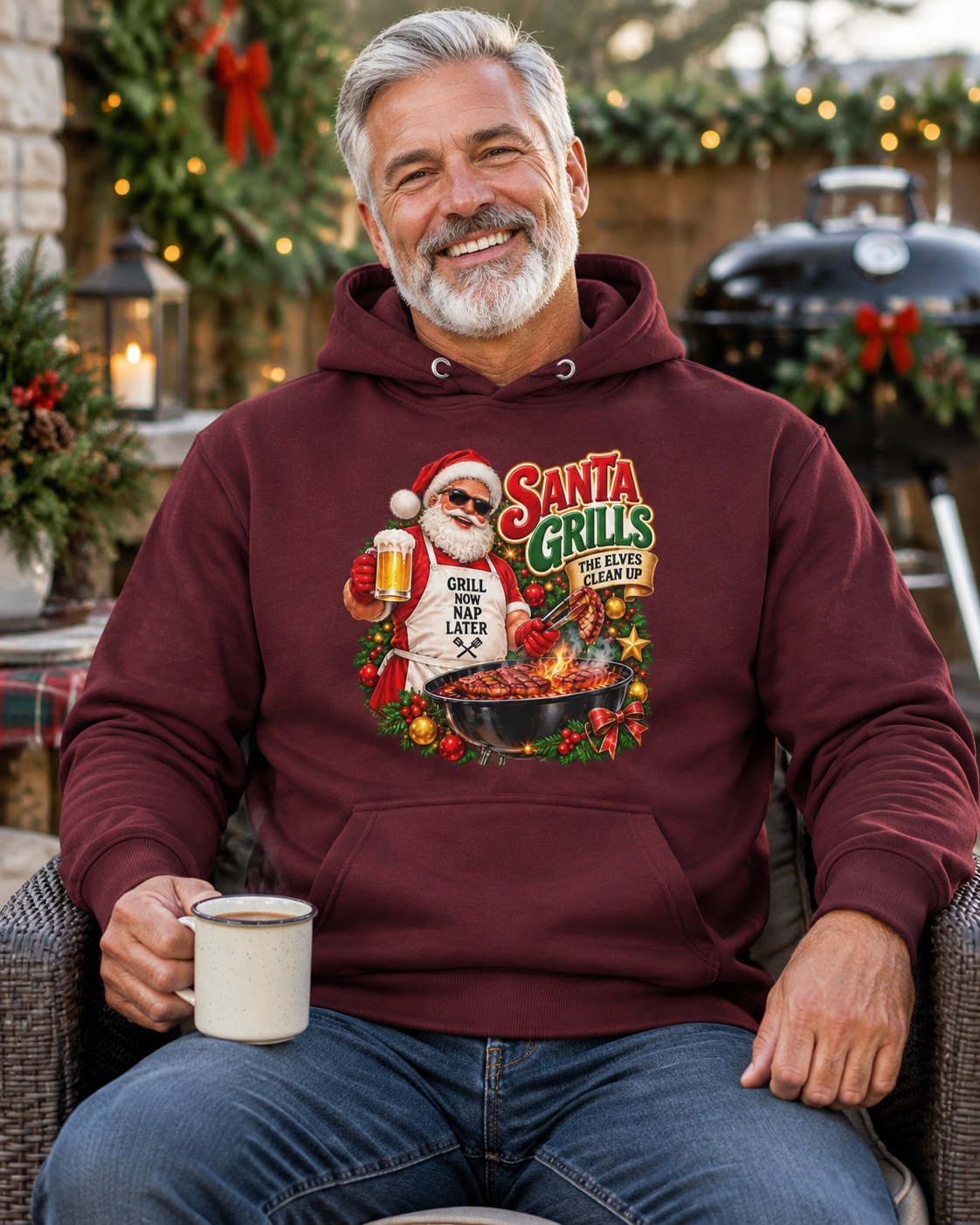 Smiling man in a maroon Santa grilling Christmas hoodie, seated with a mug on a Christmas-decorated patio