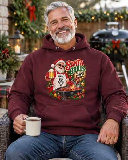 Smiling man in a maroon Santa grilling Christmas hoodie, seated with a mug on a Christmas-decorated patio