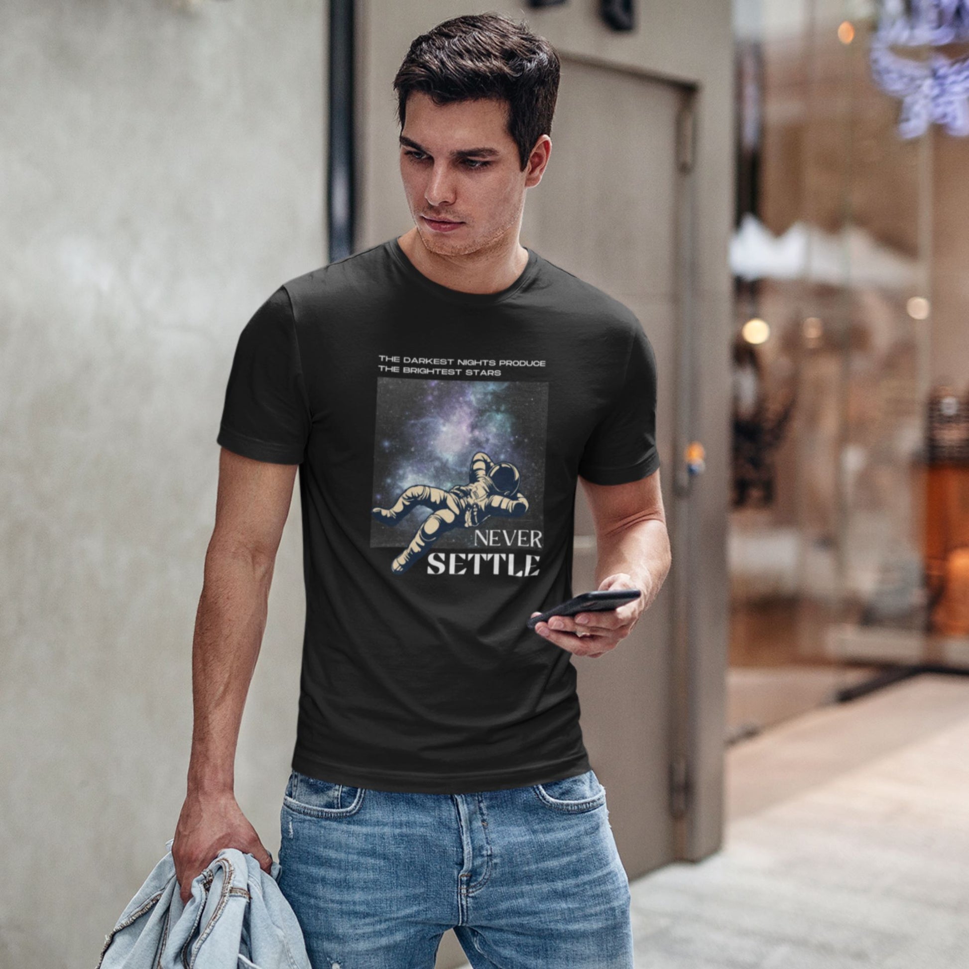 young-man-by-a-store-checking-his-phone-wearing-a-Black-t-shirt-adorned-with-Never-Settle-phrase